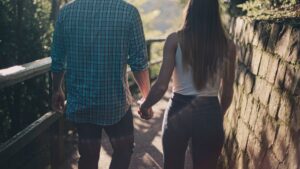 Back View Photo of Couple Holding Hands While Walking Along Pathway