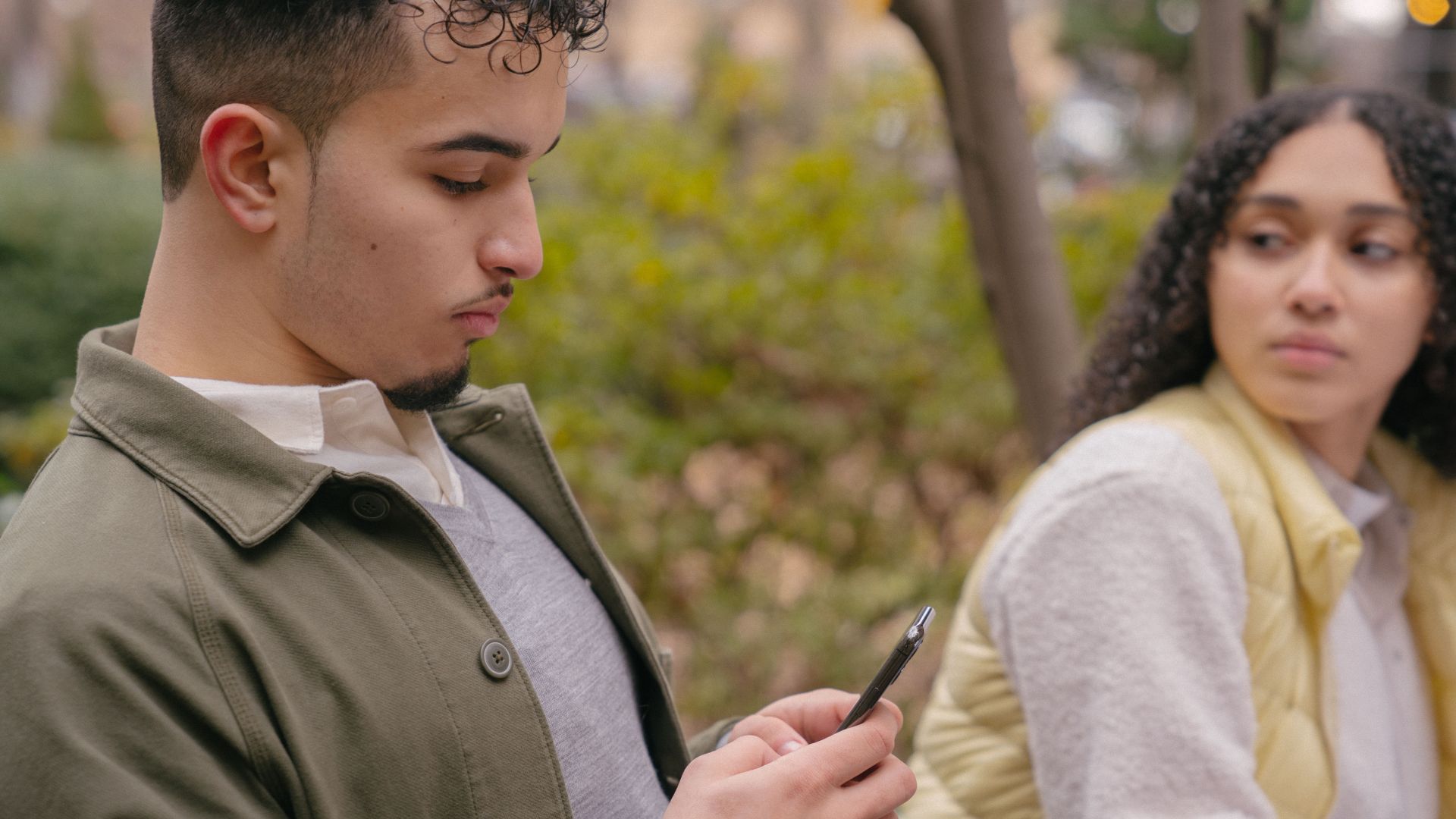 Hispanic lady looking jealously at boyfriend while texting on cellphone