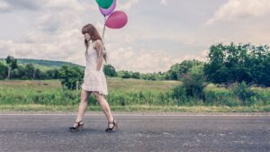 Photography of Woman Walking Near Road Holding Balloons