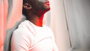 Serious black man sitting on floor near curtain