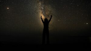 Silhouette of Person Raising Hands Under Starry Night