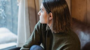 Thoughtful woman sitting on windowsill in solitude