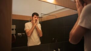 Tired man looking in mirror in bathroom