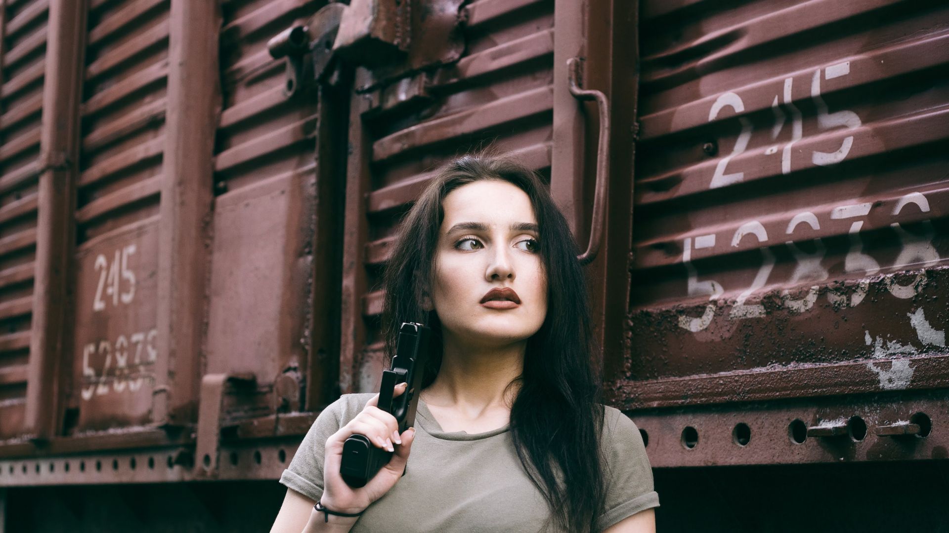 Woman Holding Black Gun while Standing beside Brown Train