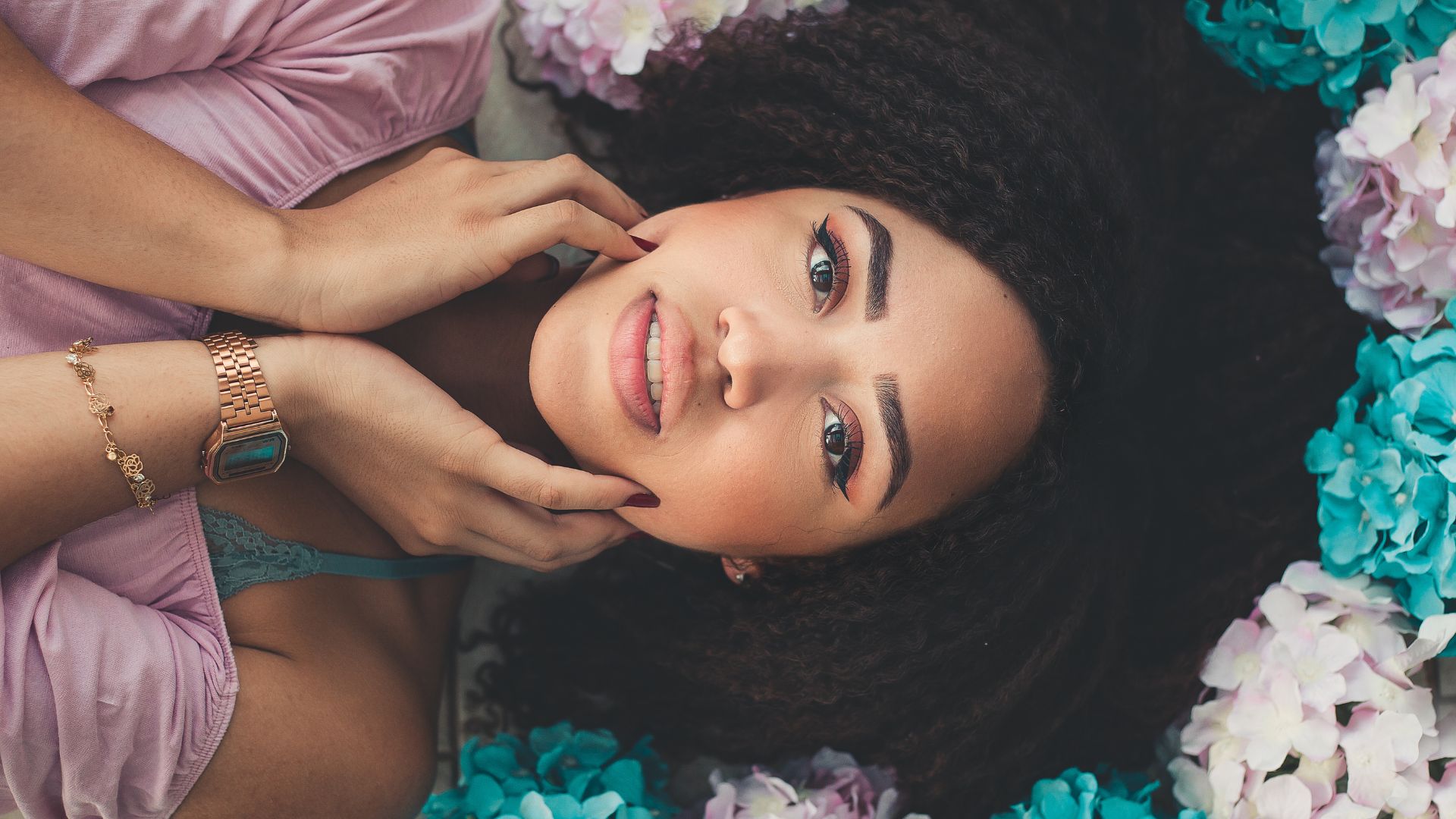 Woman Lying on White Surface With White and Teal Paper Flower Around Her Head