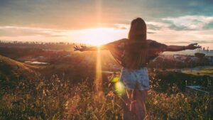 Woman Stands on Mountain over Field Under Cloudy Sky at Sunrise